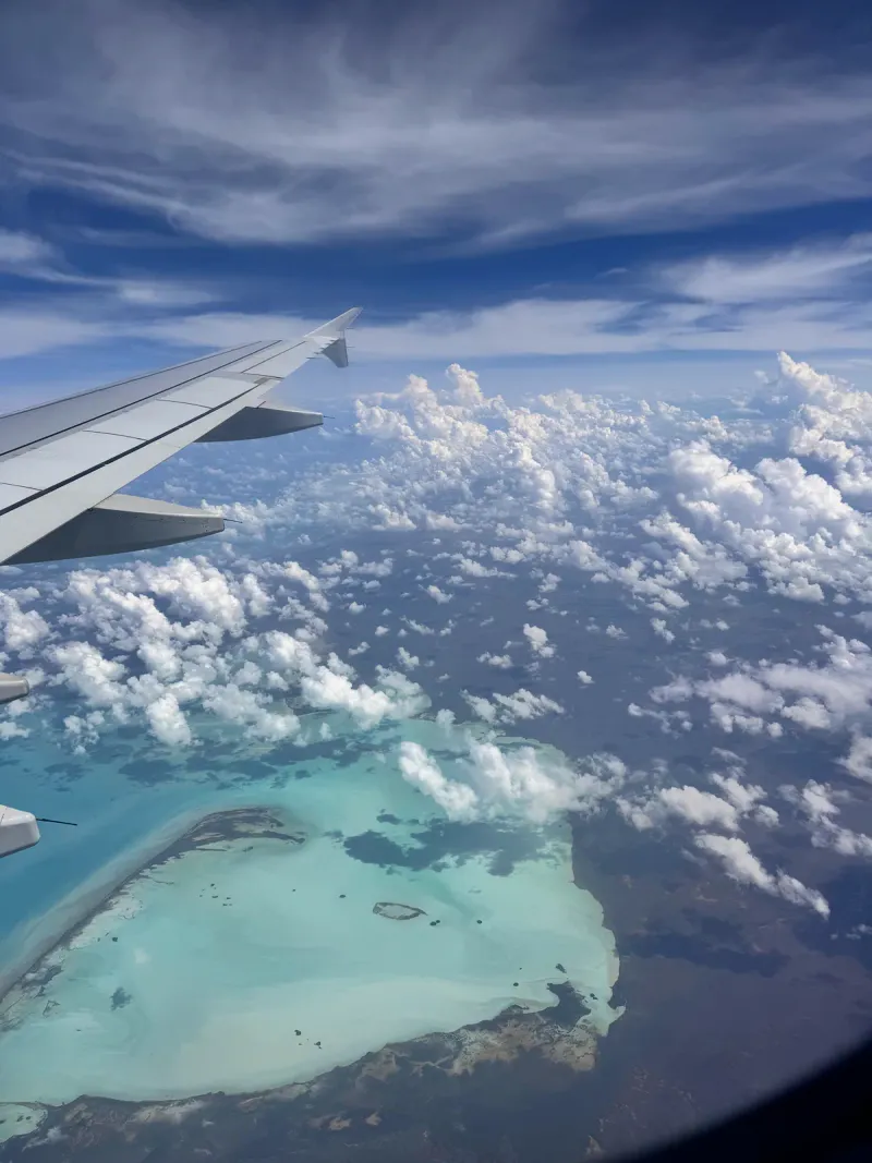 熱帯の島々の上を飛ぶ旅客機の窓から見える、ターコイズブルーの礁湖と雲