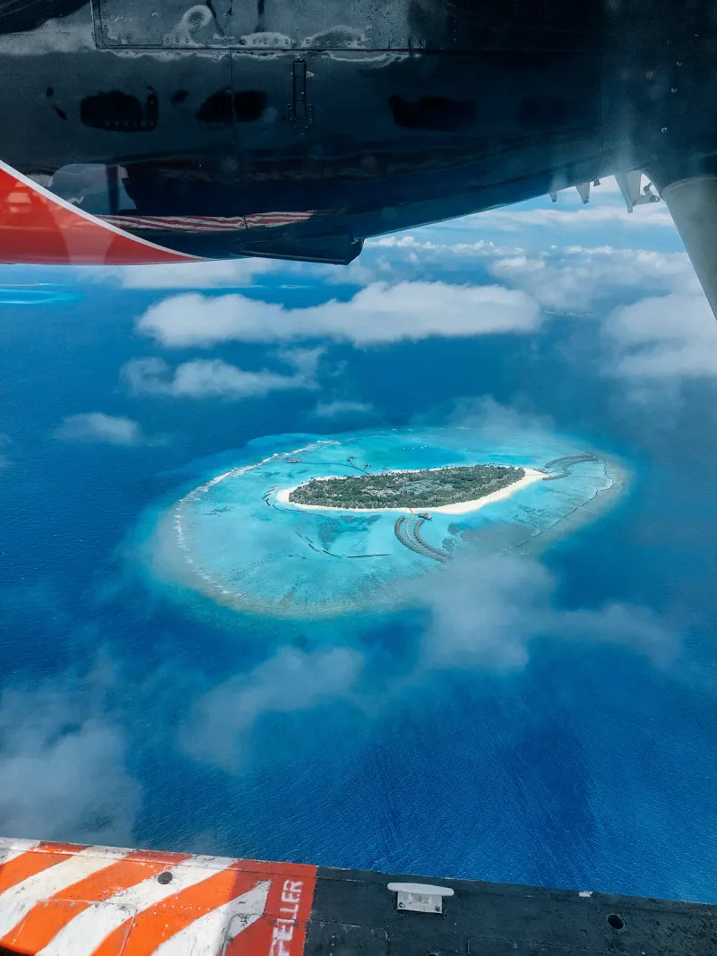 Piccola isola tropicale circondata da una barriera turchese vista dal finestrino di un aereo