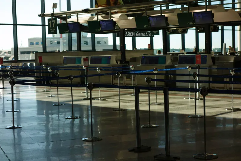 Rangée de comptoirs d'enregistrement vides dans un aéroport, avec des poteaux de file d'attente devant