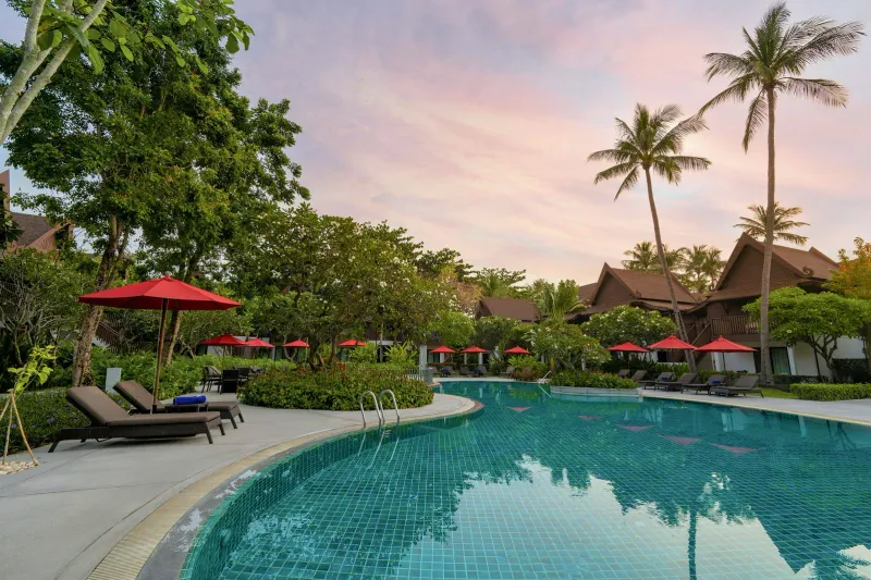 La piscina sul lungomare dell'Amari Koh Samui al tramonto, con ombrelloni rossi, palme e i tetti delle ali delle camere