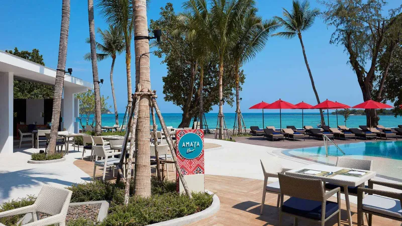 La terrazza del locale Amaya sulla spiaggia dell'Amari Koh Samui, con tavoli accanto alla piscina e ombrelloni rossi sulla sabbia