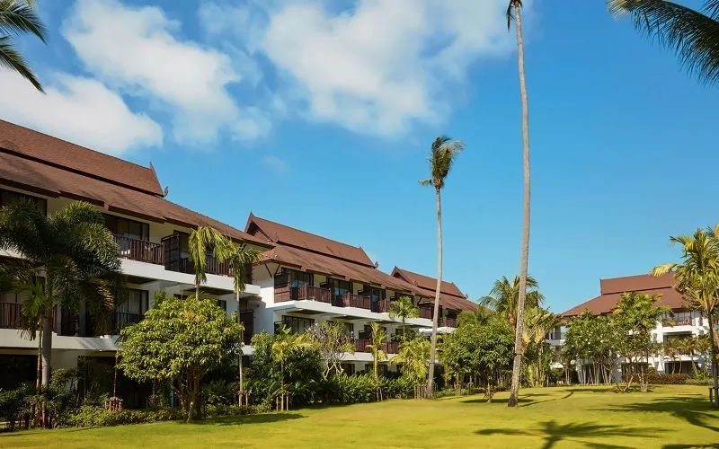 Le ali di legno delle camere dell'Amari Koh Samui e un ampio prato sotto le palme in una giornata di sole
