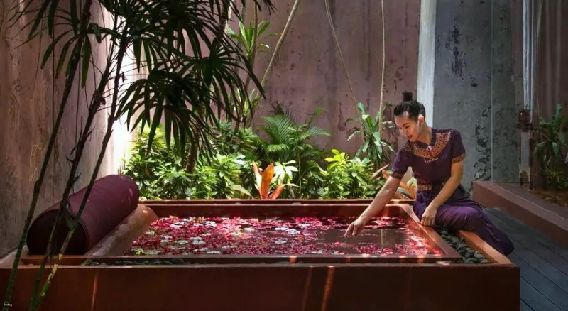 Anantara Bophut Koh Samuiのスパのパビリオンで、花の湯船に花びらを散らすセラピスト