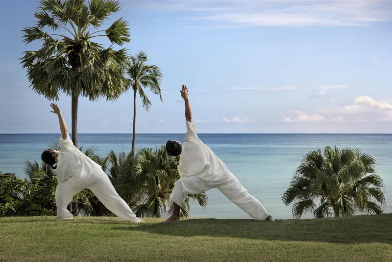 Due ospiti in bianco in posizione yoga del triangolo su un prato sopra il mare all'Anantara Lawana, Koh Samui