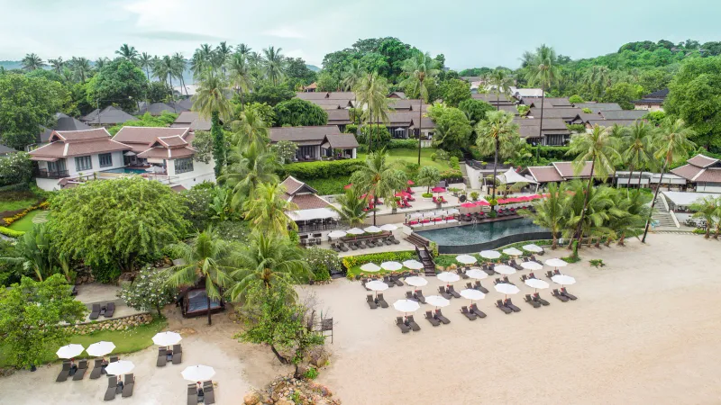 Veduta aerea dell'Anantara Lawana Koh Samui Resort con piscina sul mare, lettini e tetti in stile thailandese tra le palme