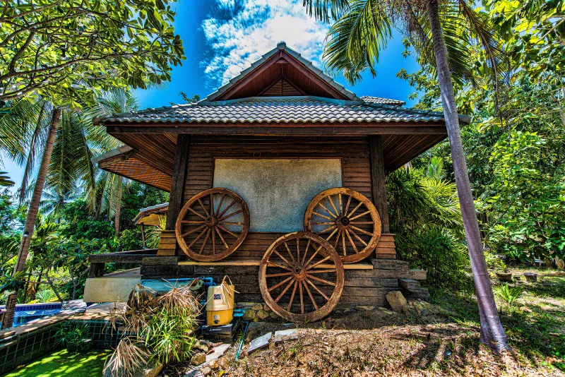 Wooden Thai-style pavilion with antique wagon wheels amid palm trees near Chaweng, Koh Samui