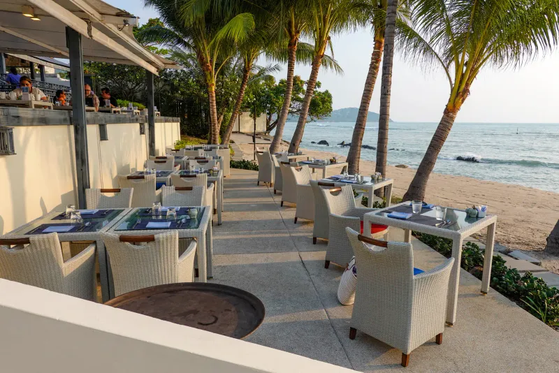 Terrazza del ristorante sul mare all'Anantara Lawana, con tavoli, sedie bianche e palme sopra l'acqua