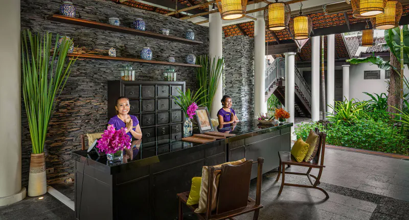 Reception della spa con parete di pietra, lanterne thailandesi e due membri dello staff all'Anantara Lawana