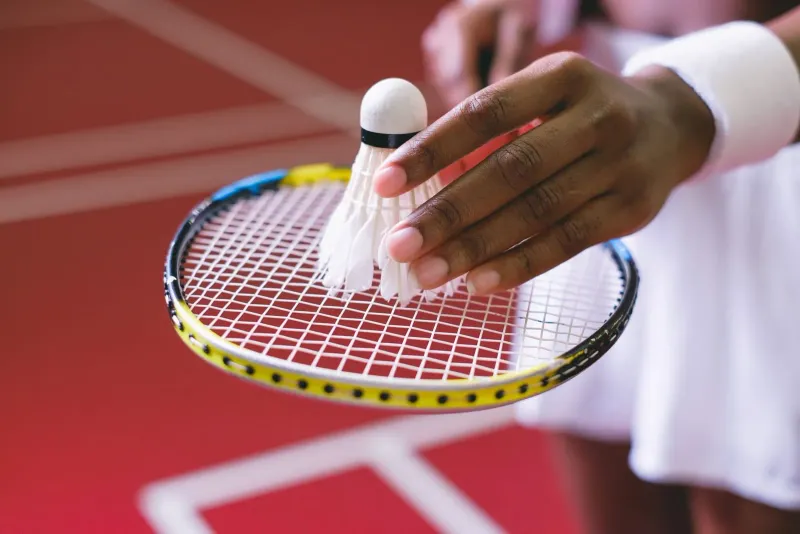 Close-up of a hand holding a shuttlecock against a badminton racket before a serve