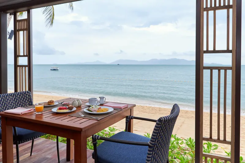 Tavolo della colazione con frutta, una frittata e succo d'arancia davanti alla spiaggia del Bandara Resort Samui