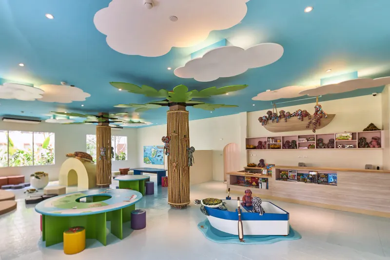 Sala giochi del Monkey Club al Bandara Resort Samui con un pilastro a forma di palma, soffitto a nuvole e una barca giocattolo