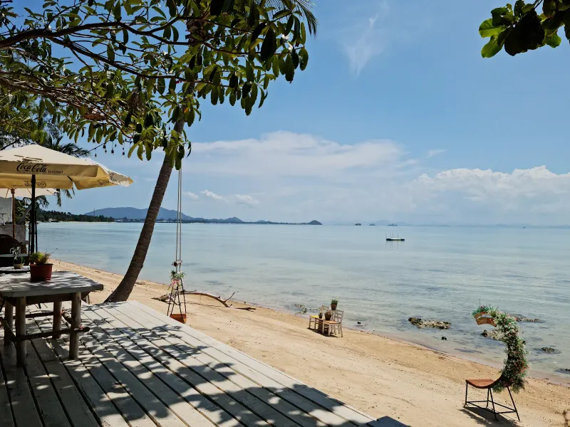 Plastikstühle und ein Sonnenschirm mit Blick aufs Wasser an einer versteckten Strandbar in Bang Makham