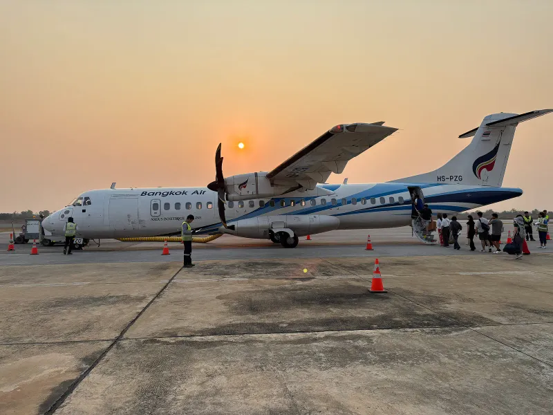 Passeggeri che salgono su un ATR 72-600 di Bangkok Airways sul piazzale di un aeroporto al tramonto