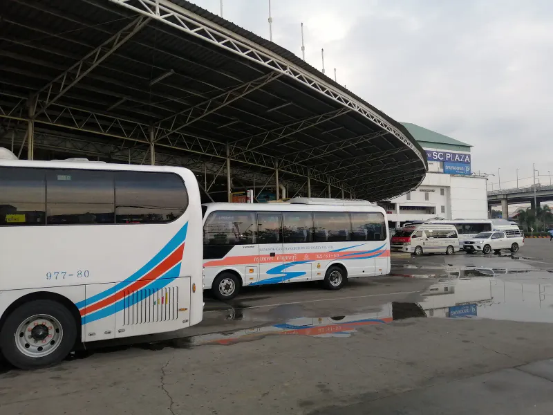 Autocars et minibus garés sous un grand hall couvert d'une gare routière de Bangkok