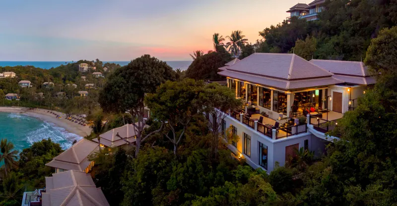 Collina del Banyan Tree Samui al tramonto con terrazze illuminate dei ristoranti sopra la baia e ville sparse