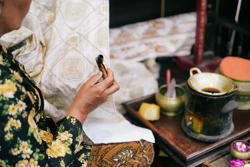 Close-up of a craftswoman applying wax to fabric during traditional batik making