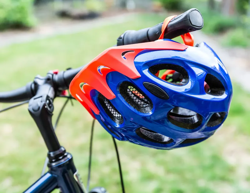 Casco da bici blu e arancione appeso al manubrio di una bici parcheggiata