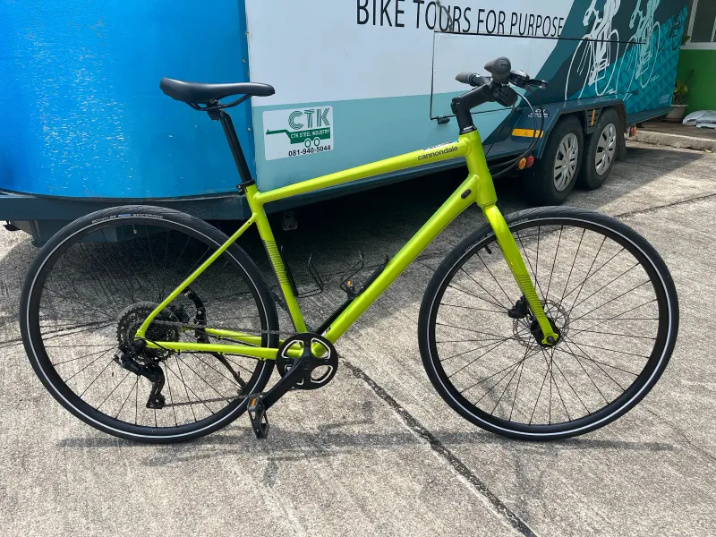 Bicicletta ibrida da città verde lime con freni a disco parcheggiata sul cemento accanto a un rimorchio per tour in bici