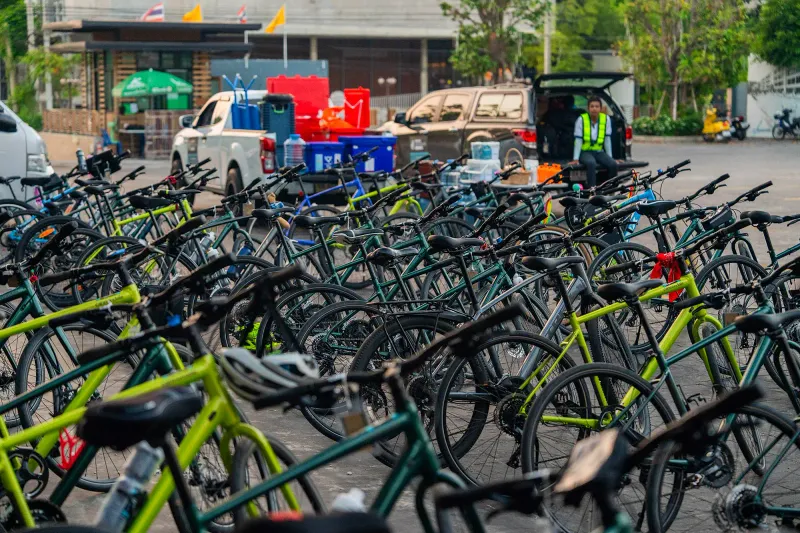 File di biciclette ibride a noleggio verdi e lime parcheggiate in un parcheggio thailandese accanto ai furgoni di supporto