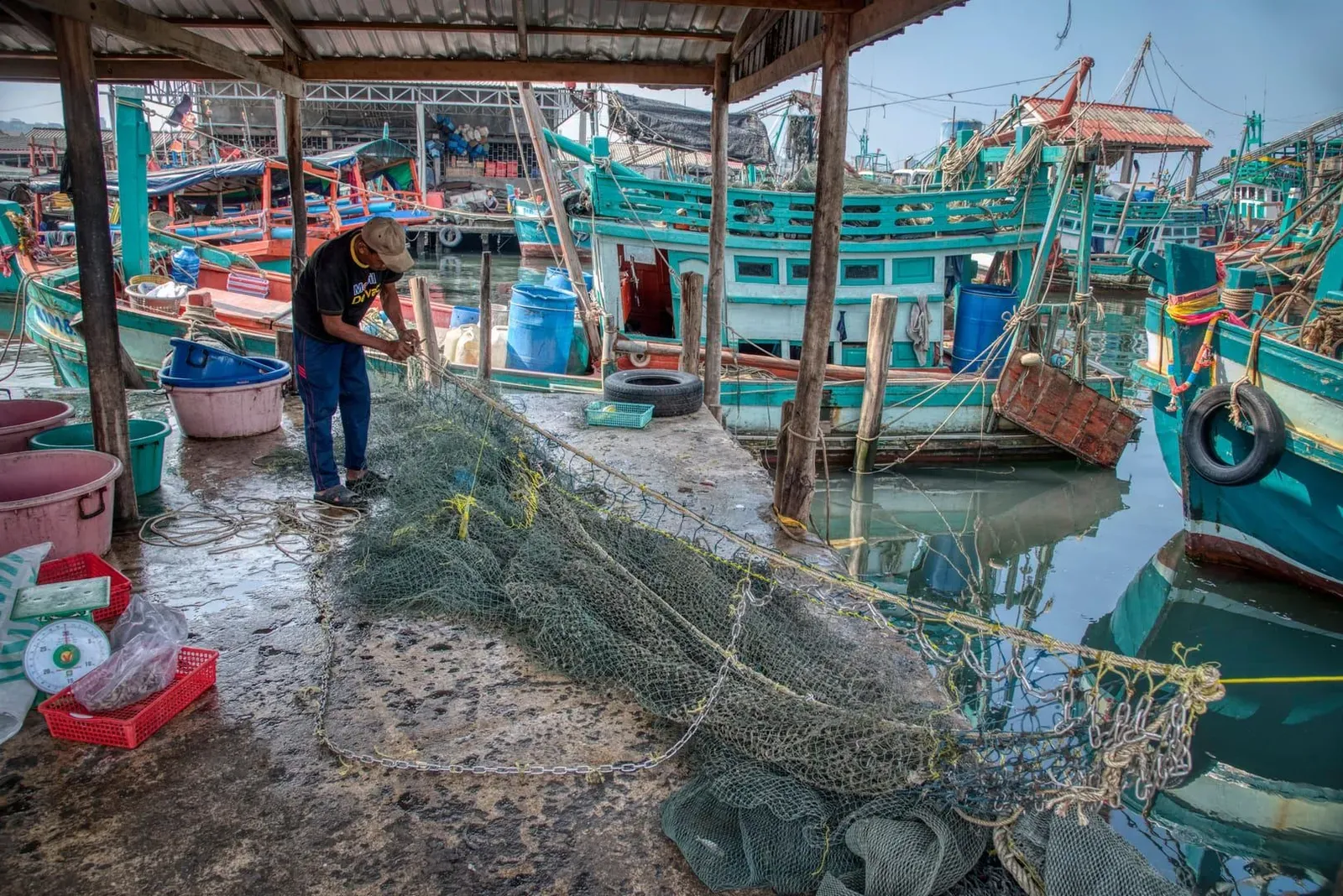 Fisherman repairing nets beside colorful longtail boats near Bophut Koh Samui harbor