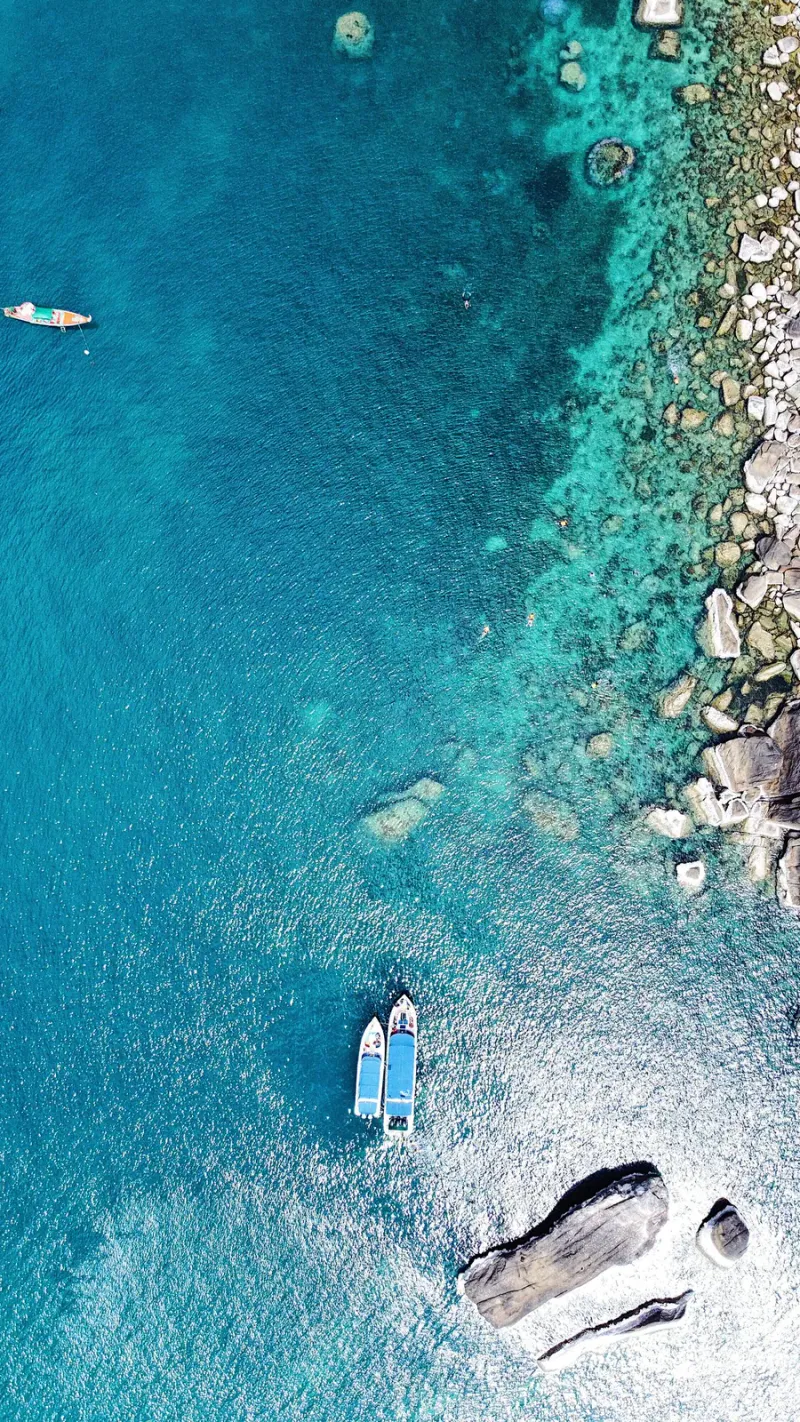 Aerial view of small boats anchored in turquoise water off a rocky Koh Samui coastline
