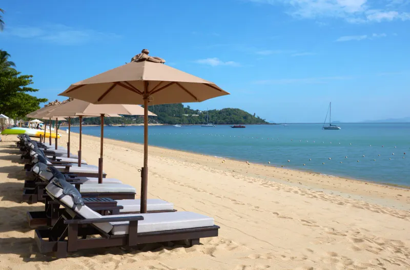 Fila di lettini e parasole sulla sabbia della spiaggia di Bo Phut, di fronte alla baia e a un piccolo promontorio