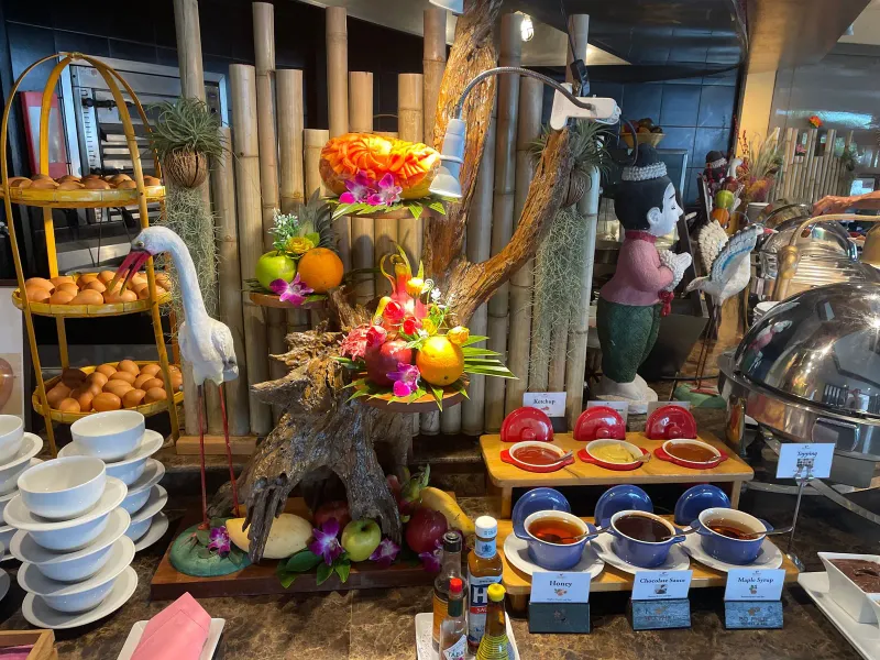 Esposizione del buffet al Bo Phut Resort and Spa con alzate di frutta a più piani, cestini di pane e marmellate in piccoli vasetti