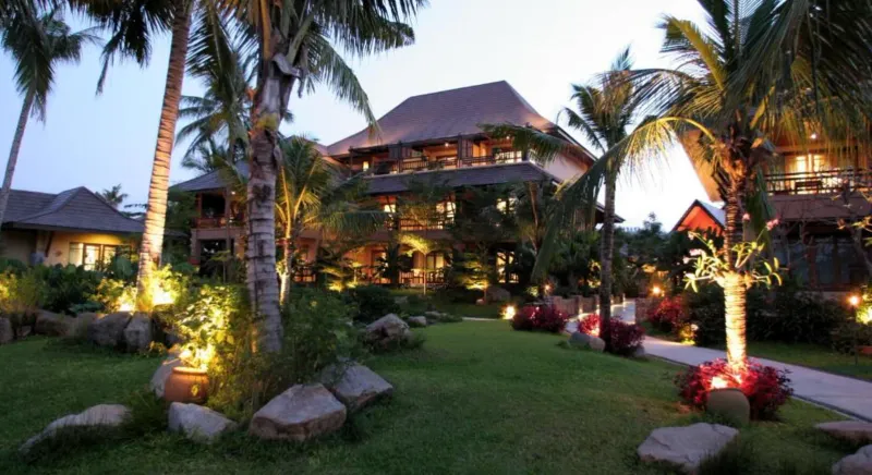 Luci serali sul prato e sul giardino di palme del Bo Phut Resort and Spa con i tetti delle ville dietro