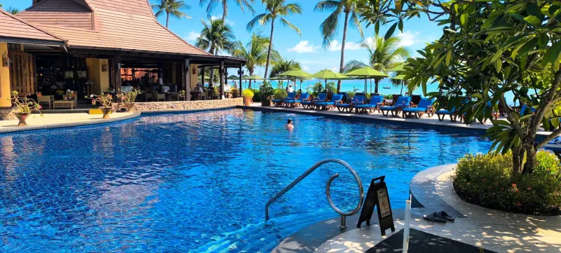 Grande piscina del Bo Phut Resort and Spa con un padiglione del ristorante dal tetto thailandese e palme sulla baia