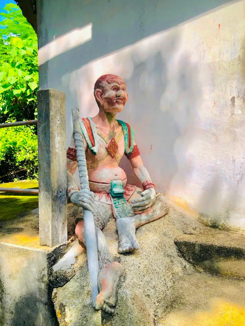 Verwitterte, bemalte Wächterstatue an der Ecke des Schreingebäudes