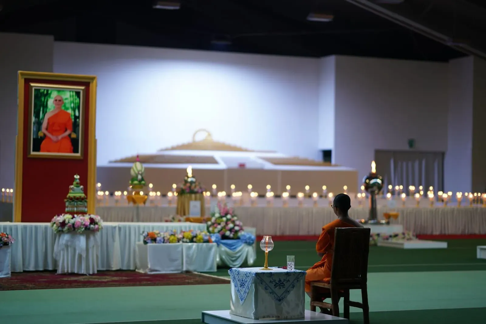 Monk seated among candles and offerings during a Buddhist ceremony marking a holy day in a Thai temple