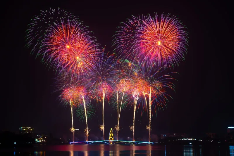 Fireworks reflecting over calm water near a beach resort during a New Year countdown