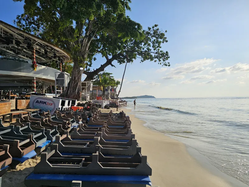 Riva sabbiosa della spiaggia di Chaweng con i lettini di un beach club impilati accanto a un grande albero