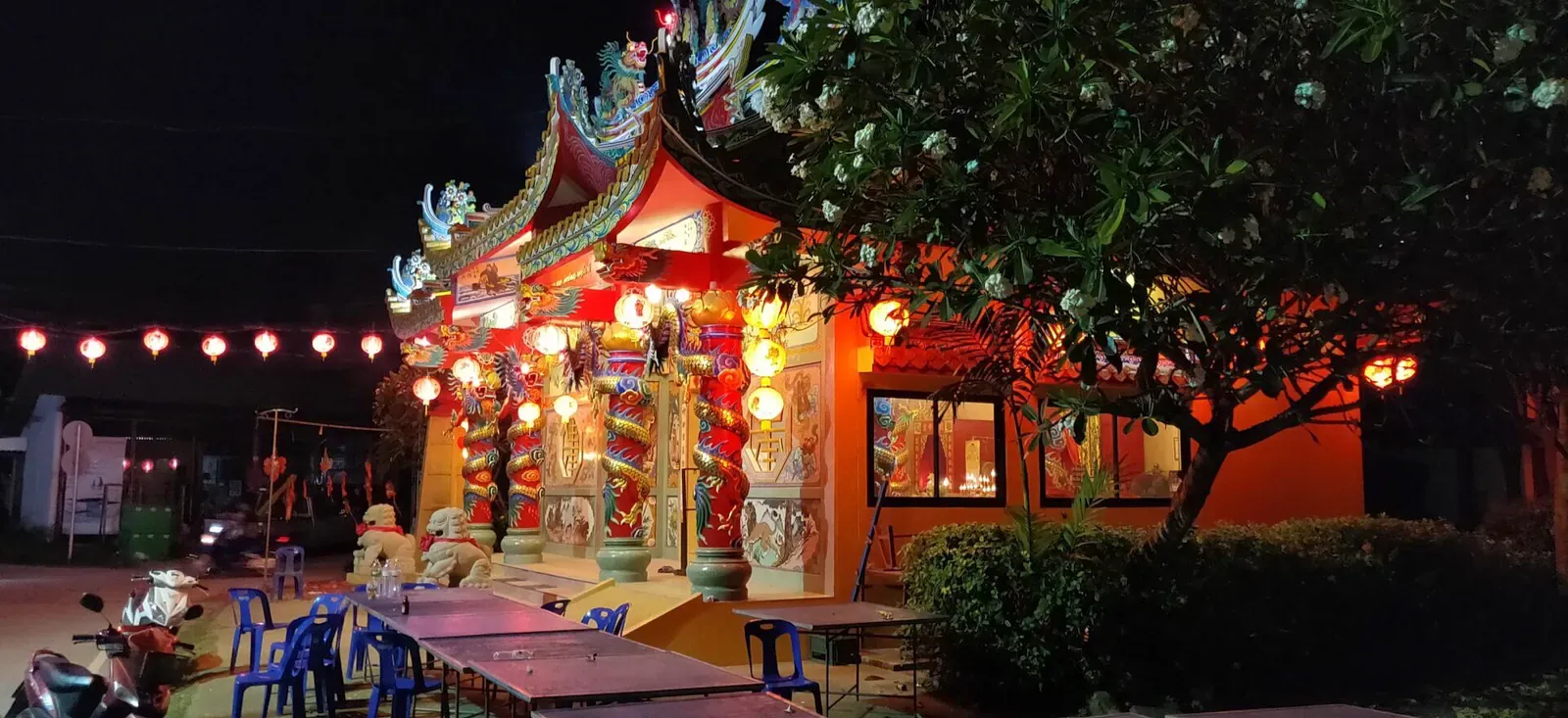 Ein chinesischer Schrein auf Koh Samui, nachts beleuchtet mit Ketten roter Laternen entlang der drachenverzierten Fassade