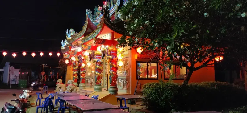 A Chinese shrine on Koh Samui lit up at night with strings of red lanterns along its dragon-carved facade