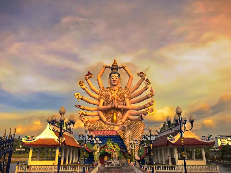 The 18-armed Guanyin statue at Wat Plai Laem silhouetted against a colourful sunset sky