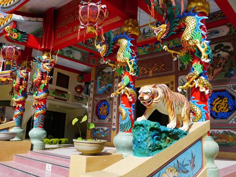 Von Drachen umschlungene rote Säulen und eine Wächter-Tigerstatue an einem chinesischen Schrein auf Koh Samui