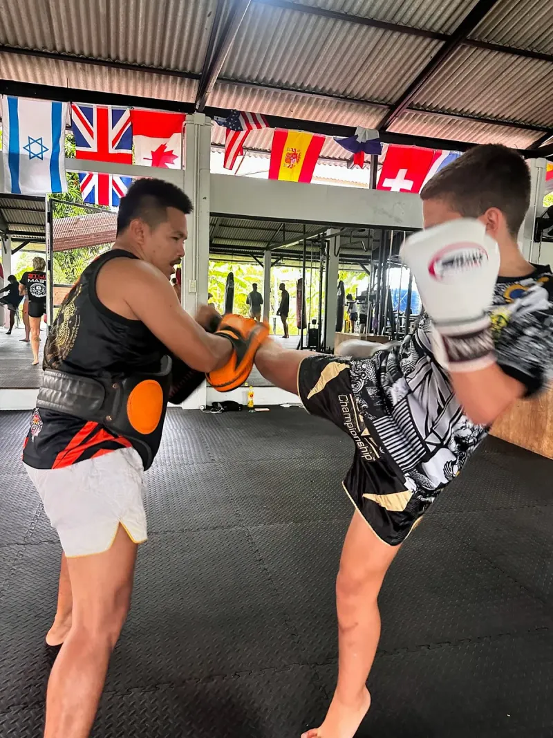 A trainer holding kick pads while a student in a white glove throws a kick