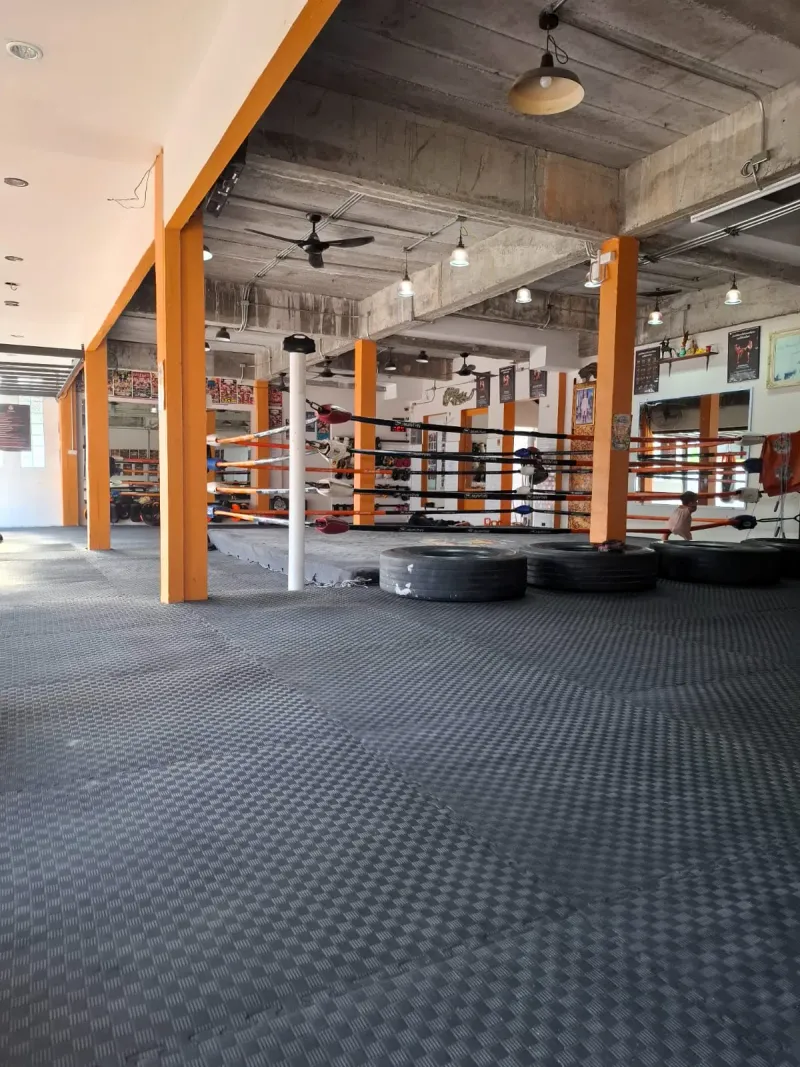 An open-air training hall with a boxing ring and tyres under orange steel columns at the Bo Phut street gym