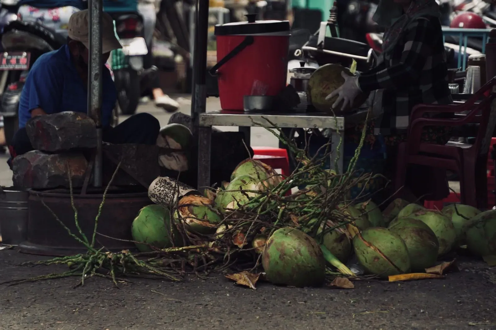 Street vendor splitting and preparing fresh coconuts by hand at an outdoor market stall in Thailand