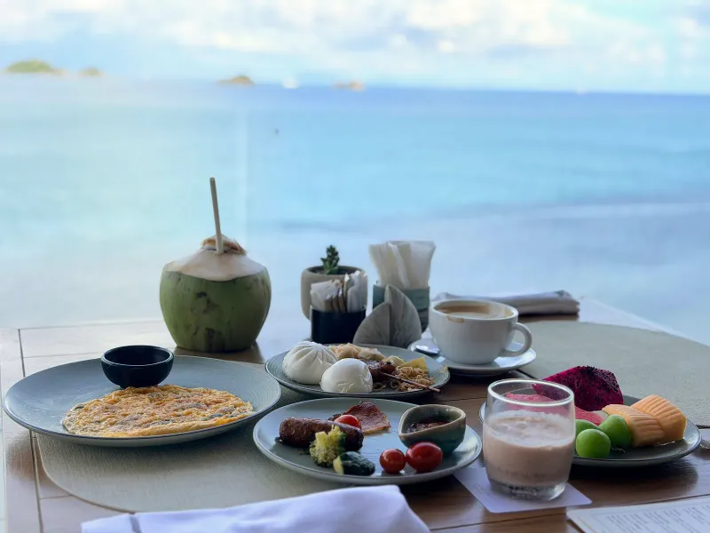 Table de petit-déjeuner avec omelette, dim sum, fruits et noix de coco face à la mer au Conrad Koh Samui