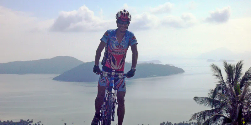 Ciclista con casco rosso in piedi sulla cima di una collina con il mare e le isole sullo sfondo