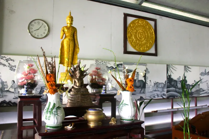 Estatua dorada de Buda de pie sobre un altar con jarrones de flores y pergaminos de caligrafía china detrás