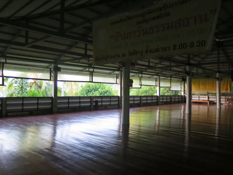 Interior del salón de meditación abierto, con tablón de anuncios y suelo de teca pulida