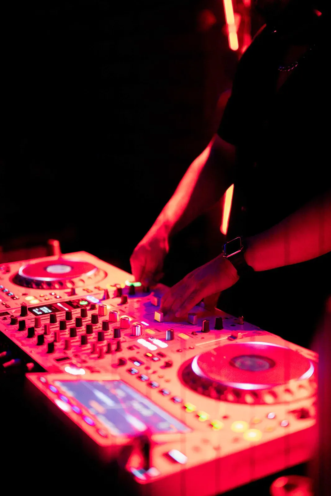 DJ hands on a mixer under red light