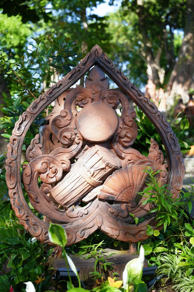 A hand-carved wooden sculpture in a tropical garden, generic illustration of the carving style displayed at Dusit Dhewa