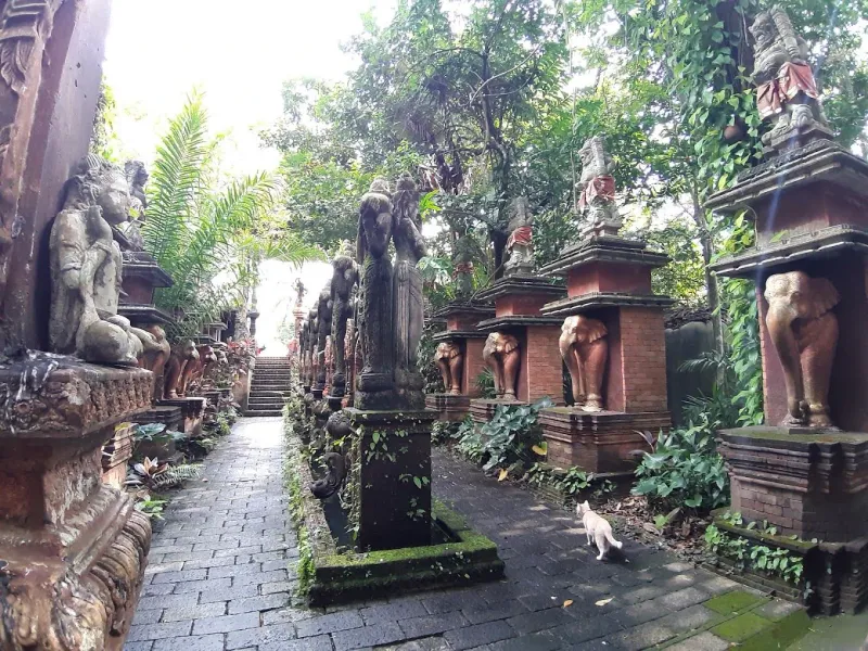 A stone avenue lined with statues and elephant carvings at Dusit Dhewa, with a cat crossing the path