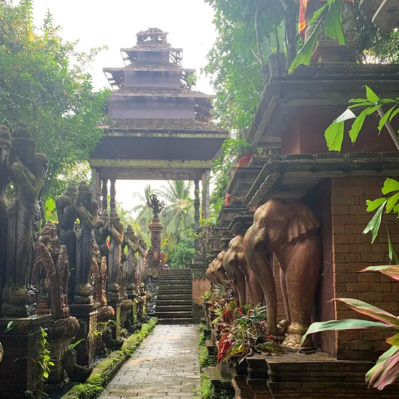 Elephant statues line a covered walkway toward a tiered pagoda roof at Dusit Dhewa