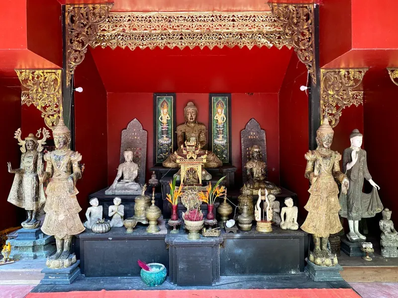 A red-walled shrine room at Dusit Dhewa filled with gilded Buddha and guardian statues