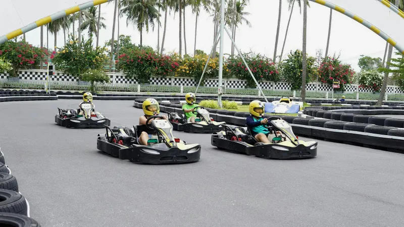 Children racing go-karts on EasyKart Koh Samui's track, with a checkered start-finish arch overhead